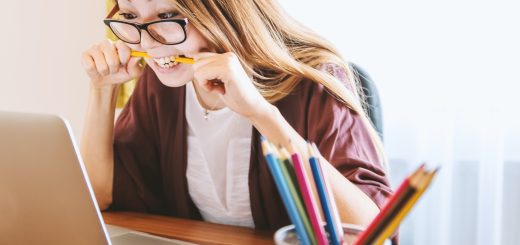 woman biting pencil while sitting on chair in front of computer during daytime
