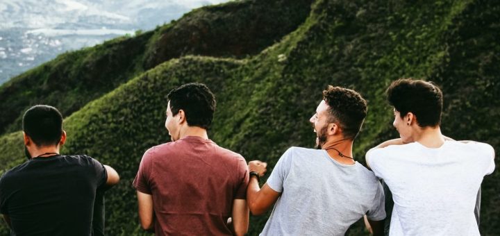 row of four men sitting on mountain trail